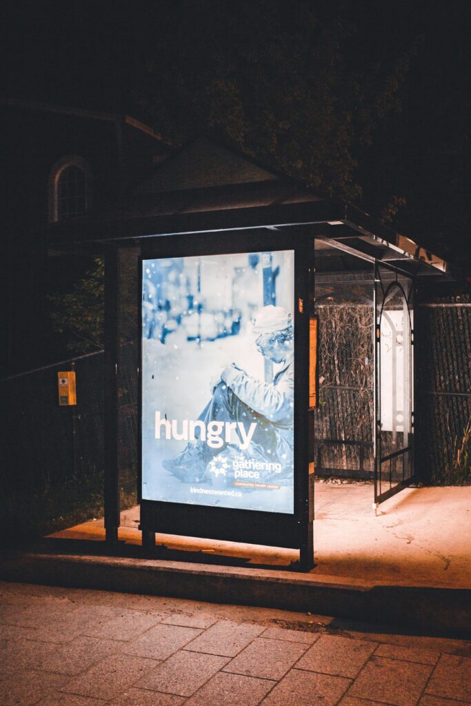 pexels-photo-12534782-12534782 A bus stop at night with an illuminated advertisement display under streetlights.