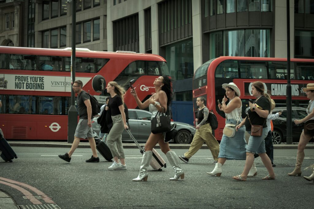 pexels-photo-27506970-27506970 Crowd crossing a London street with iconic red buses in motion, capturing urban life.